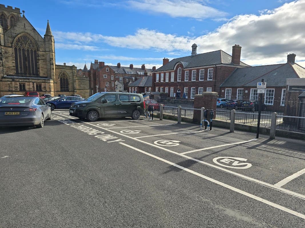 Connected Kerb Charging Station in a parking area with EV signage, near buildings and a church in Whitby, Yorkshire.