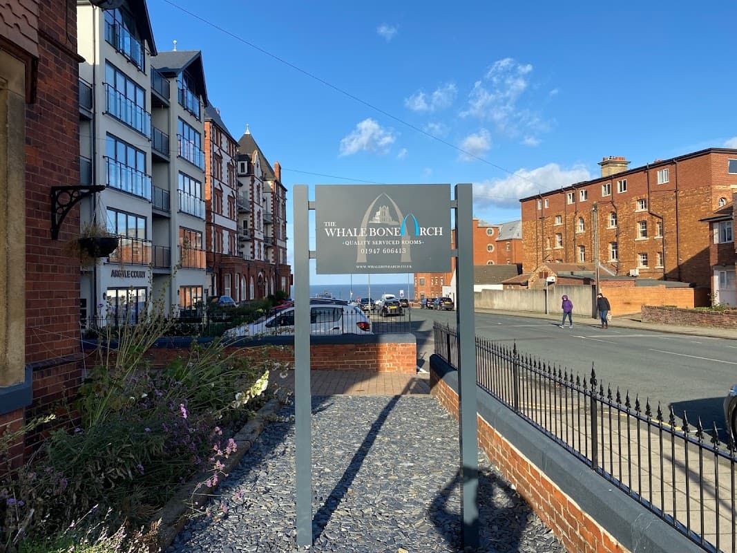 The Whalebone Arch sign in front of a hotel, with coastal views and brick buildings under a blue sky.