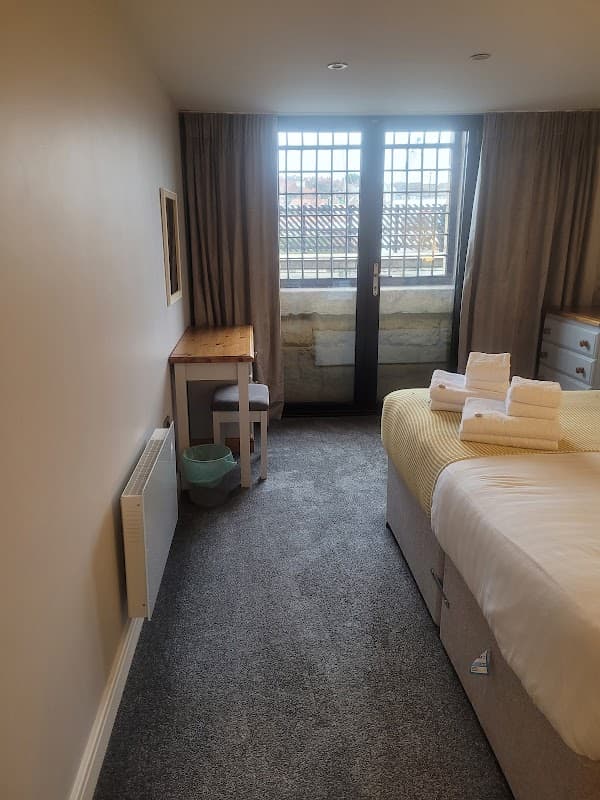 Cozy room with a bed, neatly arranged towels, a desk, chair, and large windows overlooking a scenic view.