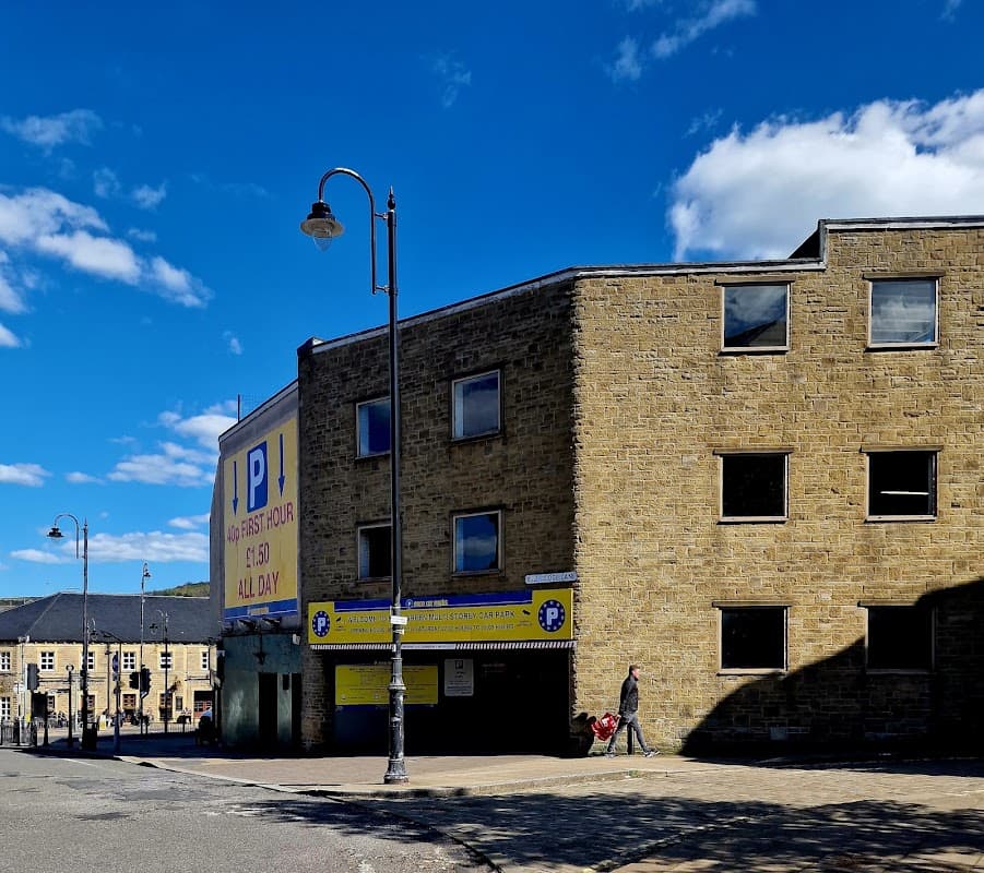 Multistory car park with yellow signage, stone walls, street lamps, and a person walking nearby under a blue sky.