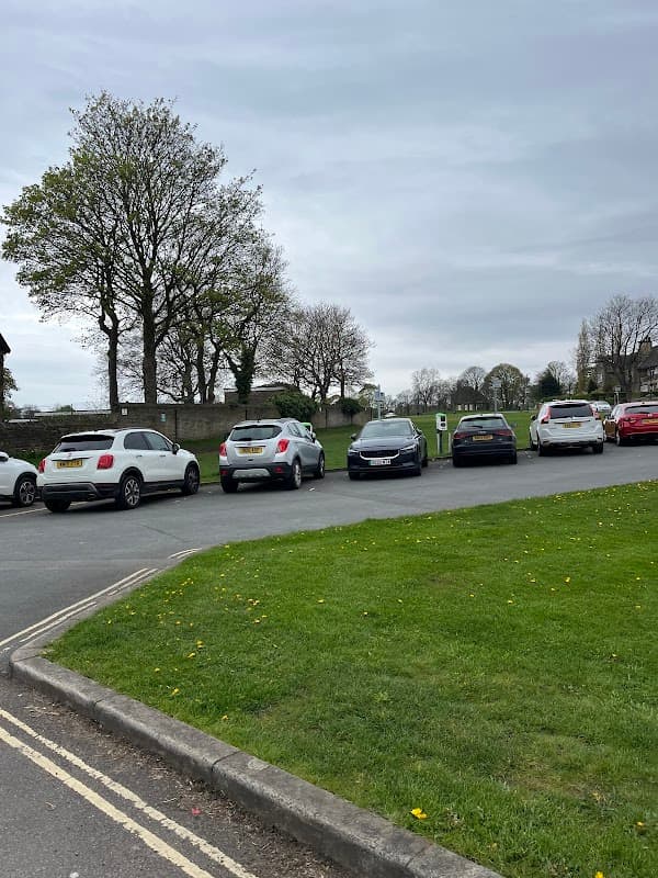 Free parking area with several parked cars, trees in the background, and grassy space in Exley, Yorkshire.