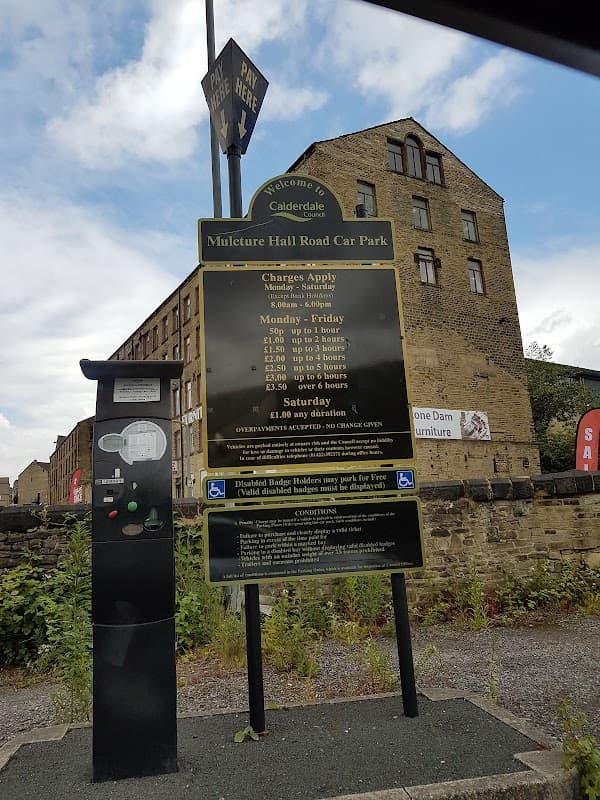 Welcome sign for Mulcture Hall Road Car Park, with payment machine and parking fees displayed, set against a brick building.