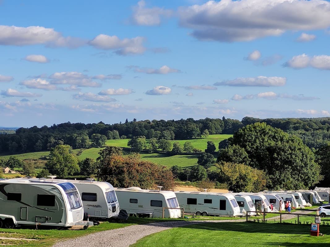 Caravans lined up on a grassy area with rolling hills and trees in the background under a blue sky with fluffy clouds.