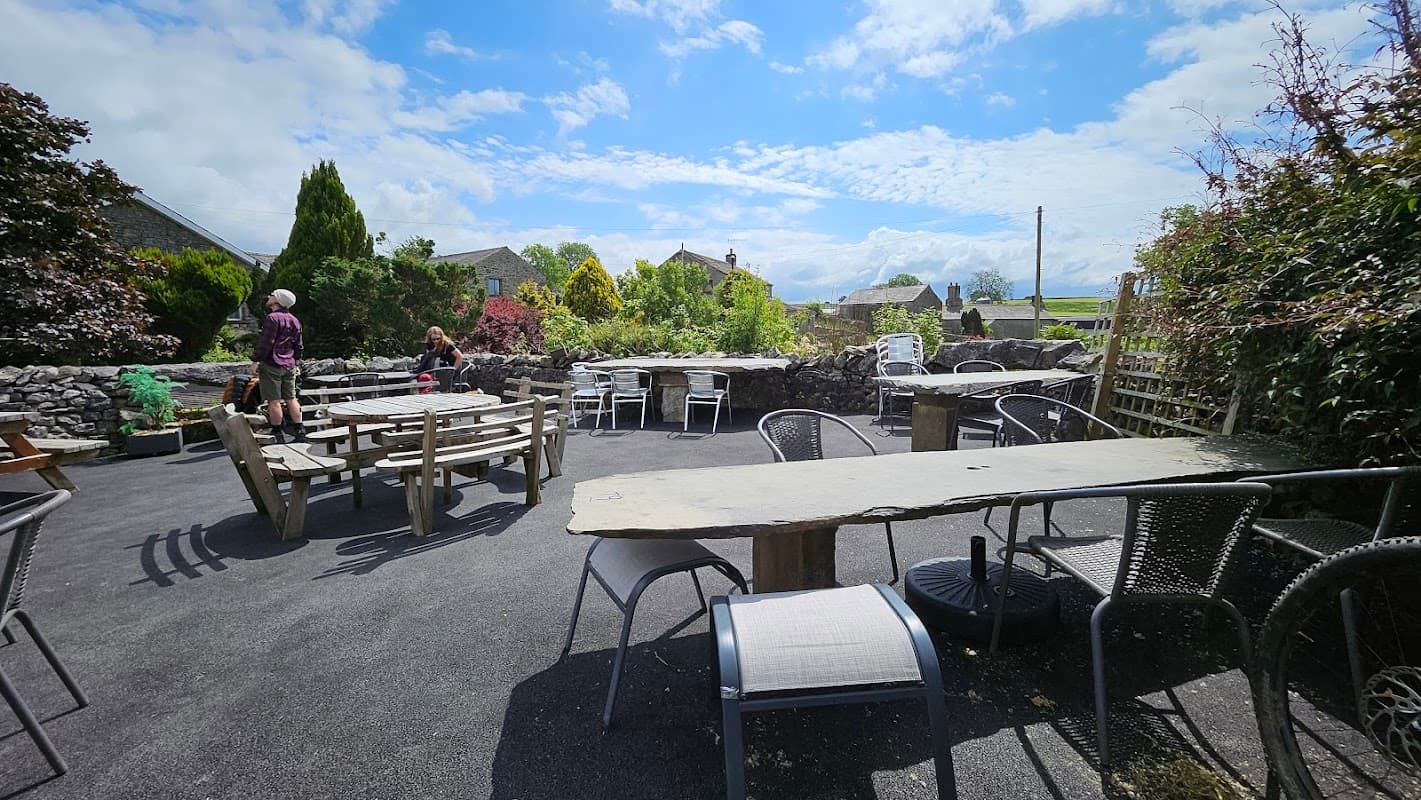 Outdoor seating area at Elaine's Tearooms, featuring stone tables, chairs, and a scenic view of greenery under a blue sky.