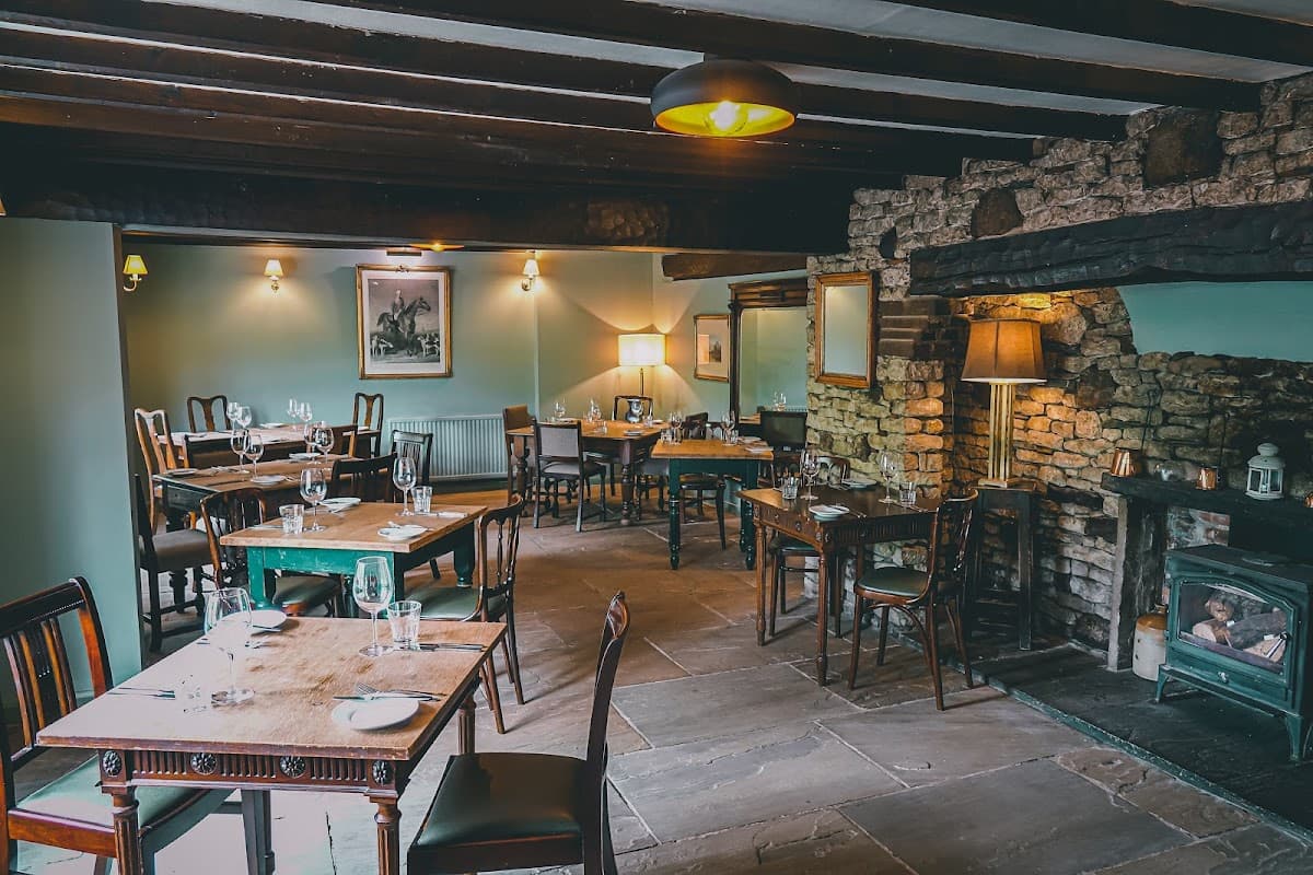 Cozy pub interior with wooden tables, chairs, stone fireplace, and soft lighting in Felixkirk, Yorkshire.