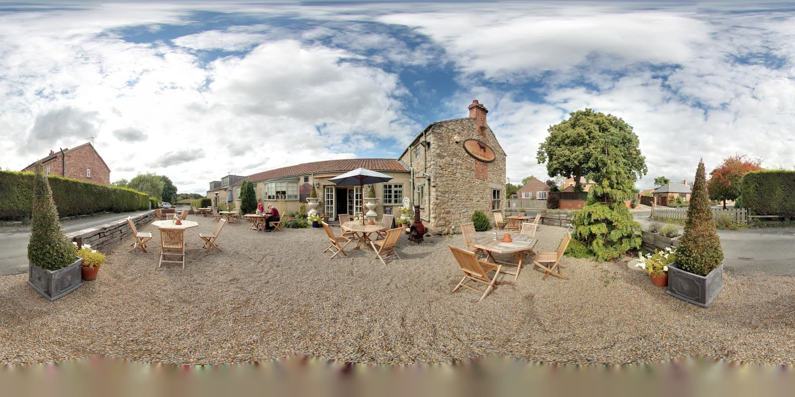 Black Horse Inn in Fencote, Yorkshire, features outdoor seating, potted plants, and a charming stone building under a cloudy sky.