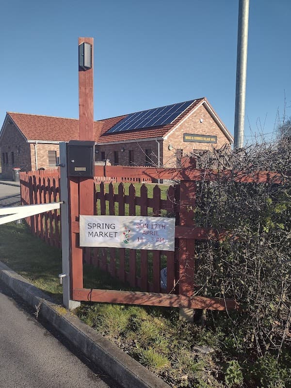 Moss and Fenwick village hall with solar panels, a wooden fence, and a sign for the Spring Market event.