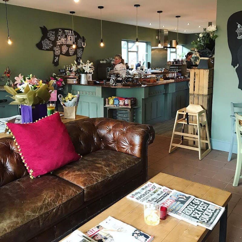 Cozy cafe interior with a leather sofa, wooden tables, flowers, and a bustling counter in a warm, inviting atmosphere.