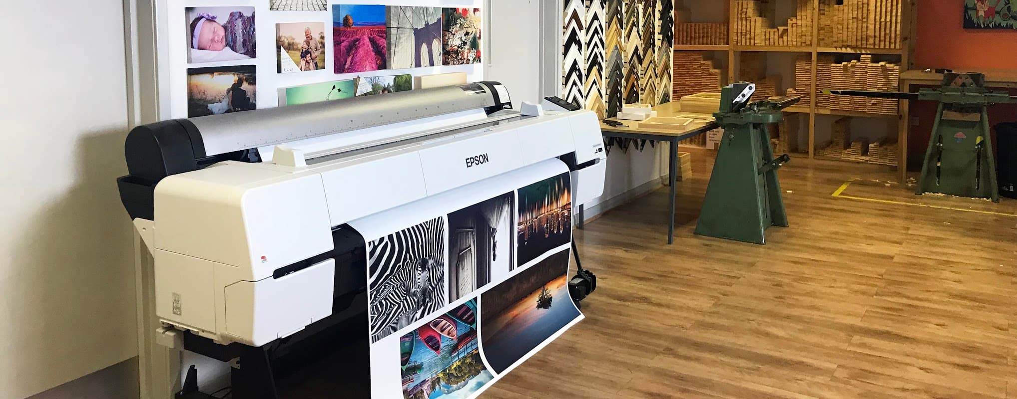 Large printer displaying vibrant images, with wooden shelves and tools in a well-lit workspace.