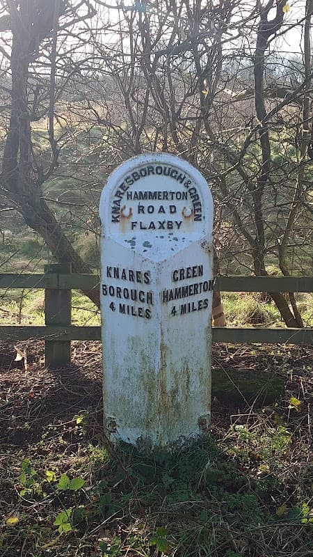 Weathered stone milestone with distances to Knaresborough, Green Hammerton, and Flaxby, surrounded by trees.