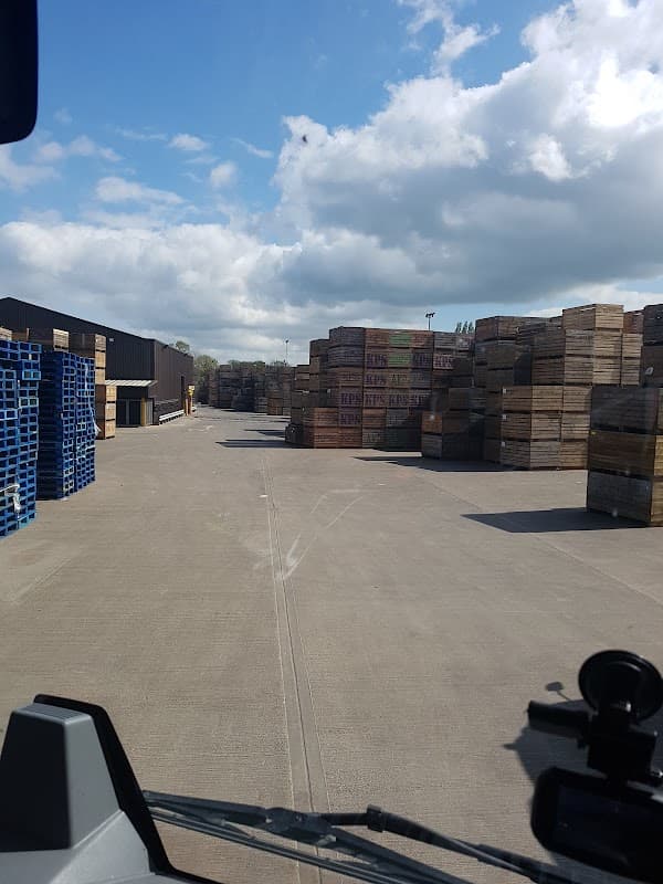 Stacks of wooden pallets and crates lined along a concrete pathway under a partly cloudy sky at a produce facility.