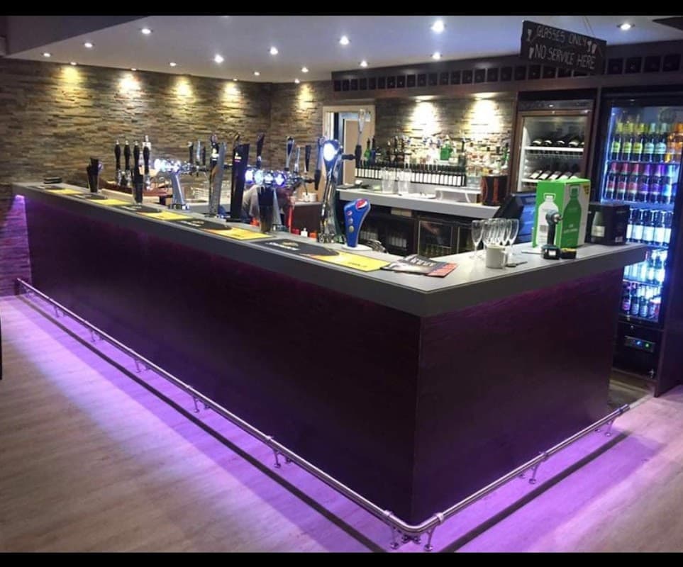 Modern bar with a sleek counter, illuminated taps, and shelves stocked with drinks in a cozy setting.