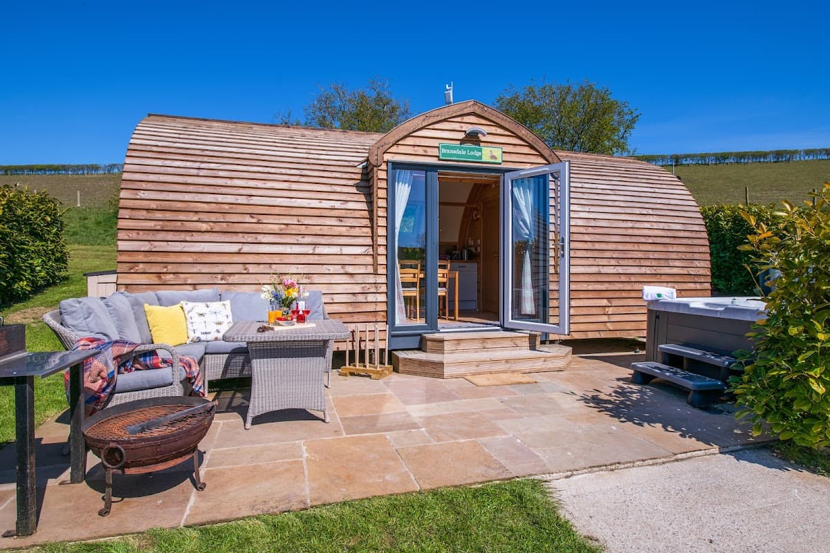 Charming wooden glamping pod with patio seating, surrounded by greenery under a clear blue sky in Folkton, Yorkshire.