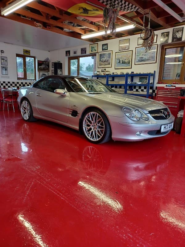 Silver Mercedes sports car parked in a bright red garage with checkered decor and framed automotive artwork.