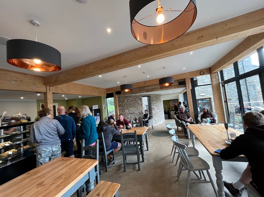 Modern café interior with wooden beams, tables, and customers enjoying food and drinks in a cozy atmosphere.