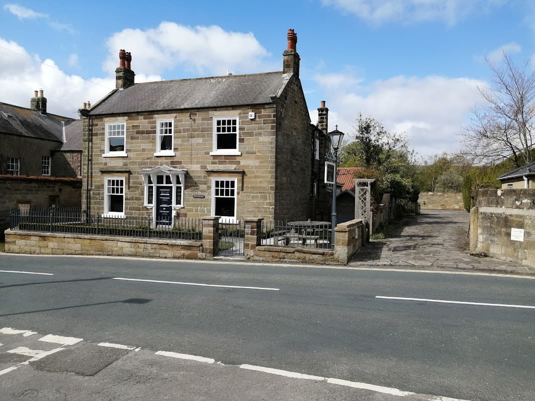 Stone hotel with a fenced front yard, large windows, and a driveway, set against a blue sky in Yorkshire.