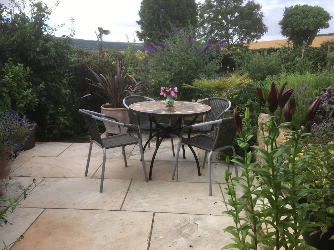 Charming outdoor seating area with a round table and chairs surrounded by lush greenery and colorful flowers.