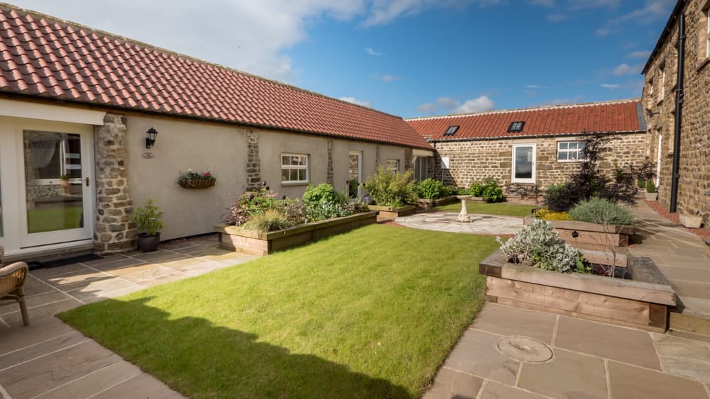 Charming courtyard at Holme Grange Farm with stone buildings, lush greenery, and a sunny blue sky in Galphay, Yorkshire.