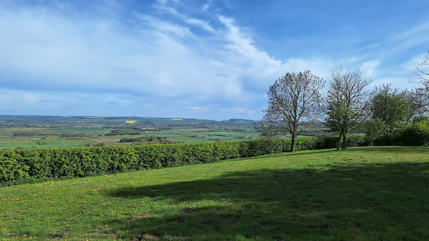 Pay & Display parking area with a view of rolling green hills, trees, and a blue sky in Ganton, Yorkshire.