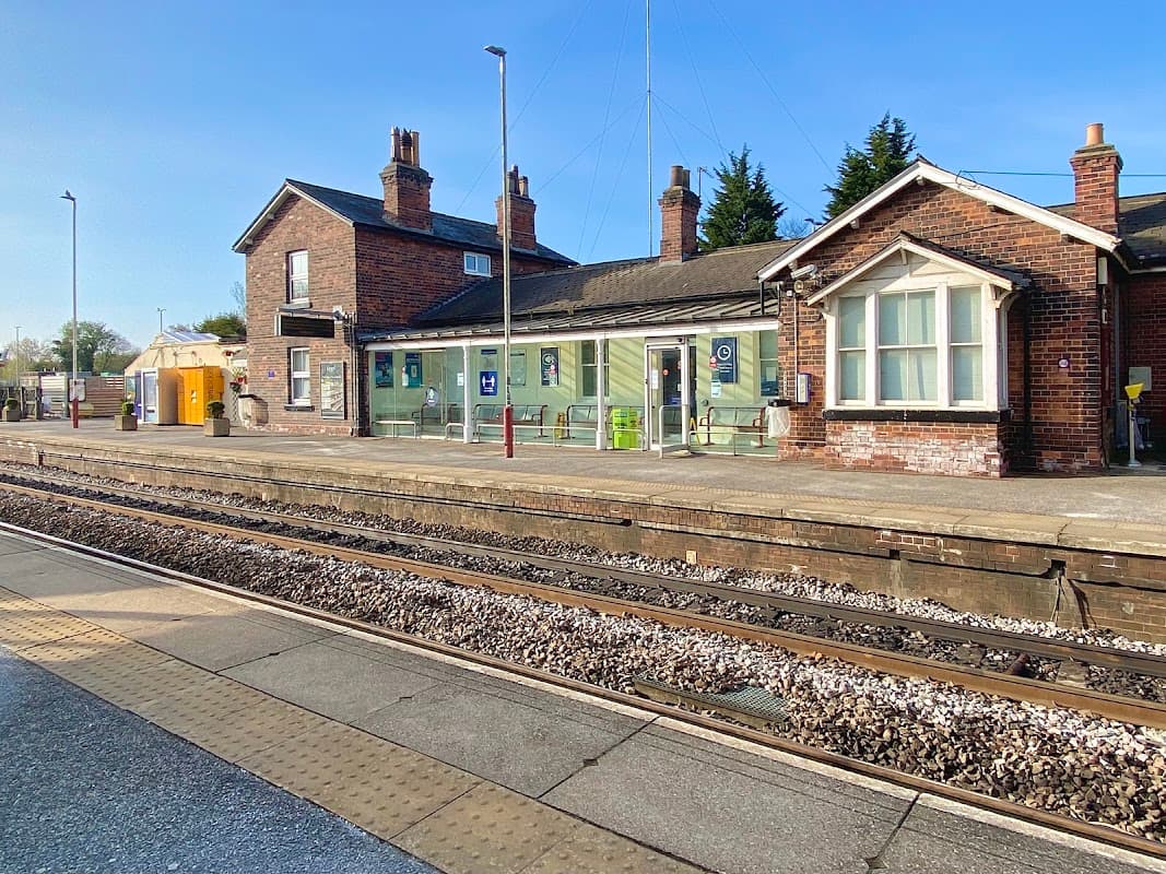 Garforth station building with brick faΓ§ade, green signage, and platforms beside railway tracks under a clear blue sky.