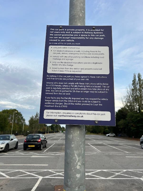 Sign on a pole detailing parking rules for Garforth Station Car Park, with empty parking spaces in the background.