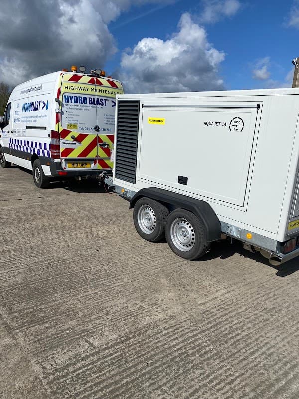 Hydroblast Limited van and a trailer-mounted pressure washer on a concrete surface under a partly cloudy sky.