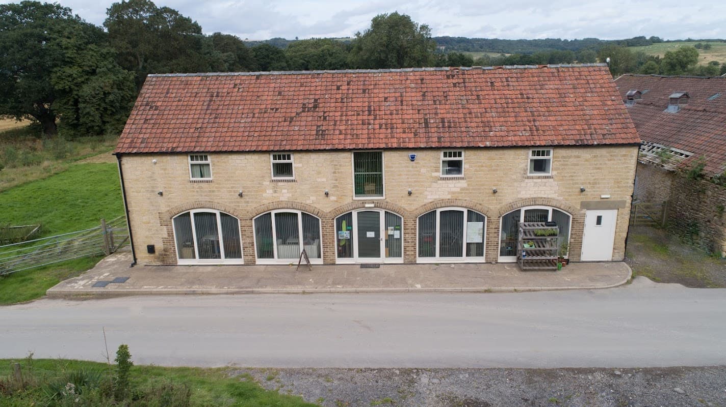 Stone building with arched windows, a red-tiled roof, and a sign for Park House Barns, set in a rural landscape.