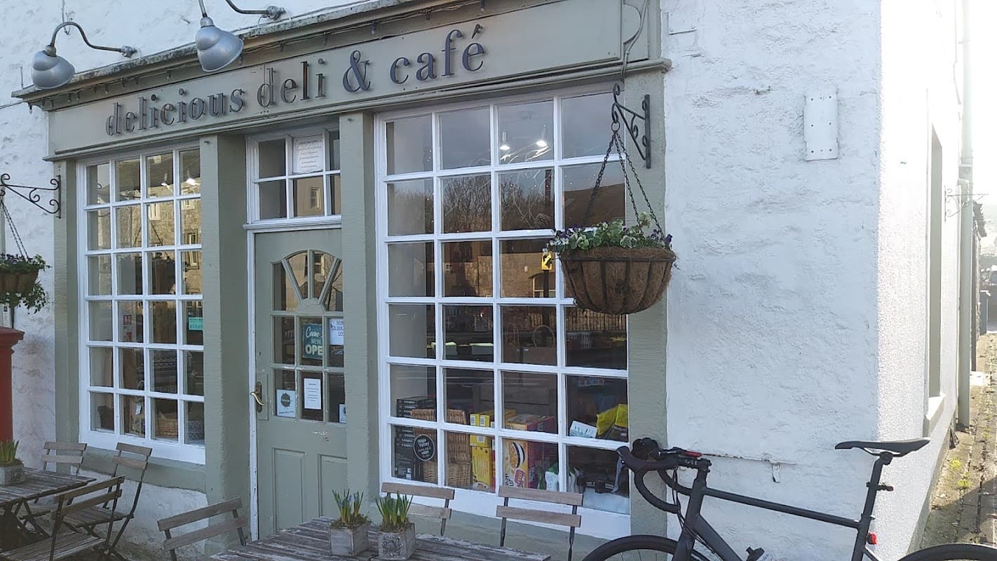 Charming deli and café with large windows, hanging planters, outdoor seating, and a bicycle parked outside.