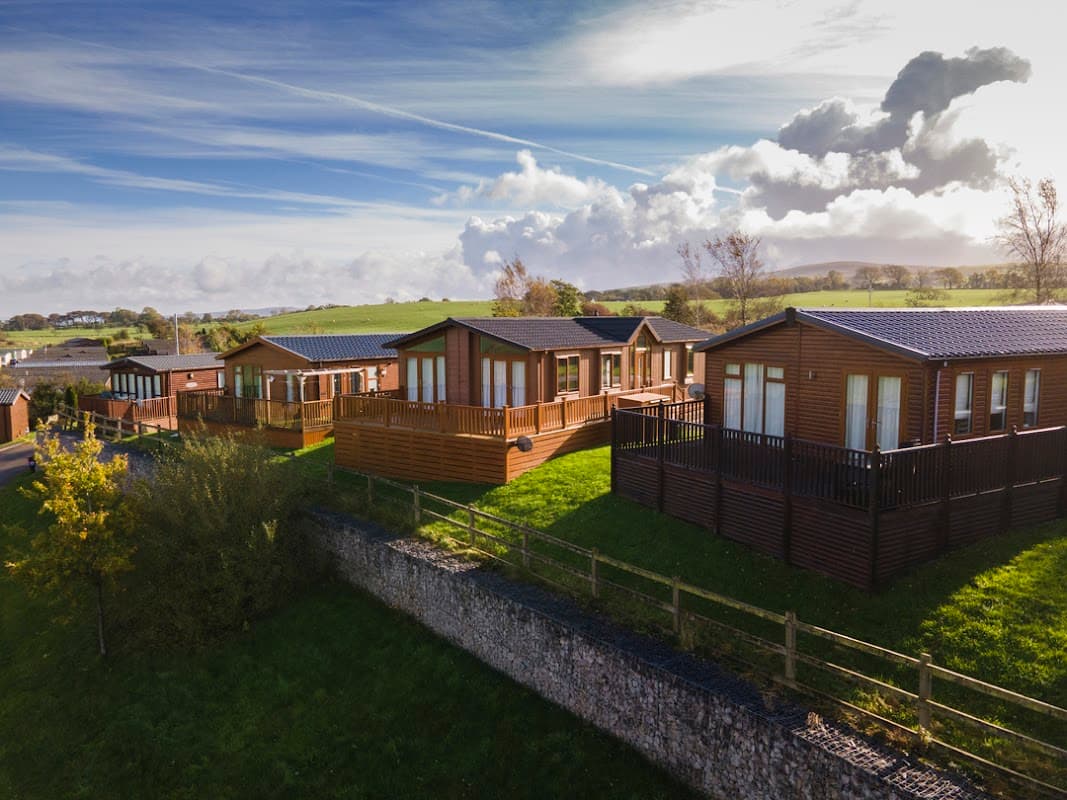 Lodges with wooden exteriors on green hills, surrounded by trees and a blue sky with fluffy clouds at Todber Valley.