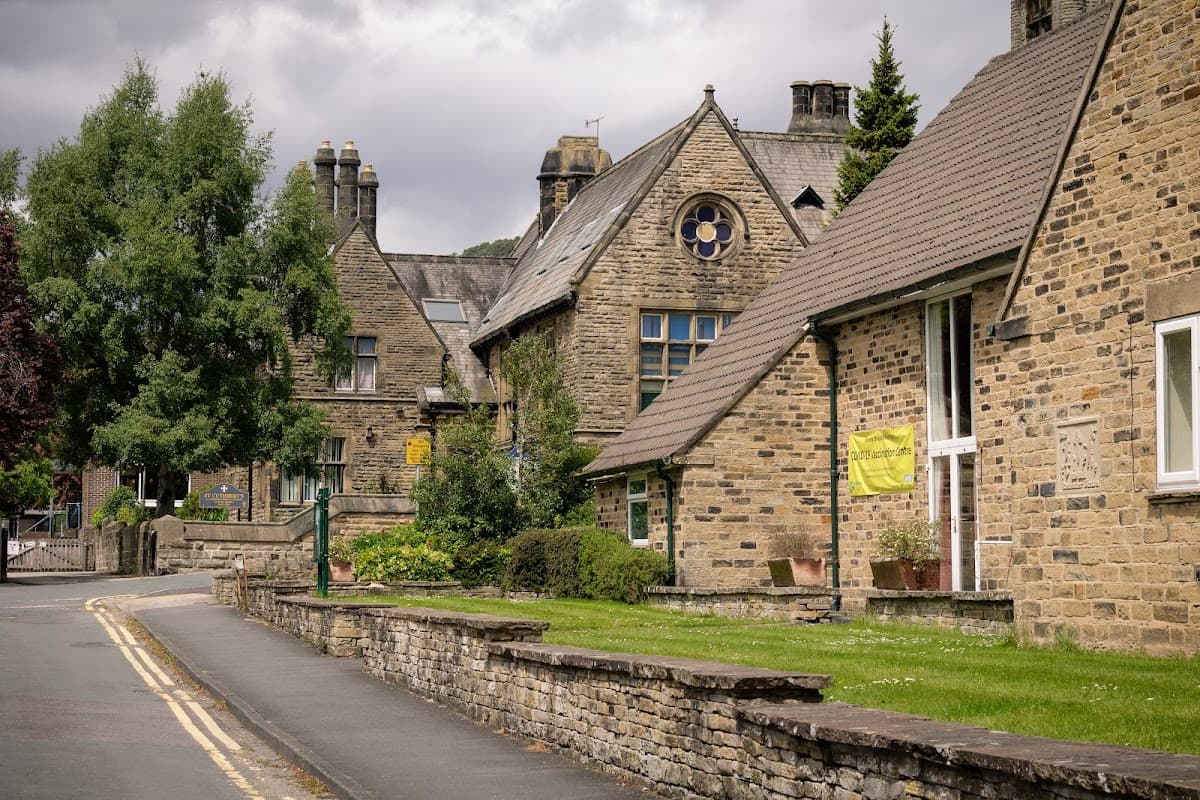 Historic stone buildings line a quiet street, with green trees and a memorial hall featuring a round window.