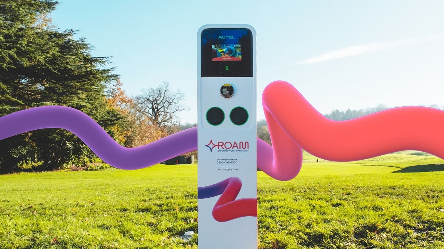 Roam Charging Station in a grassy area, featuring a sleek white design with colorful abstract elements and a screen.