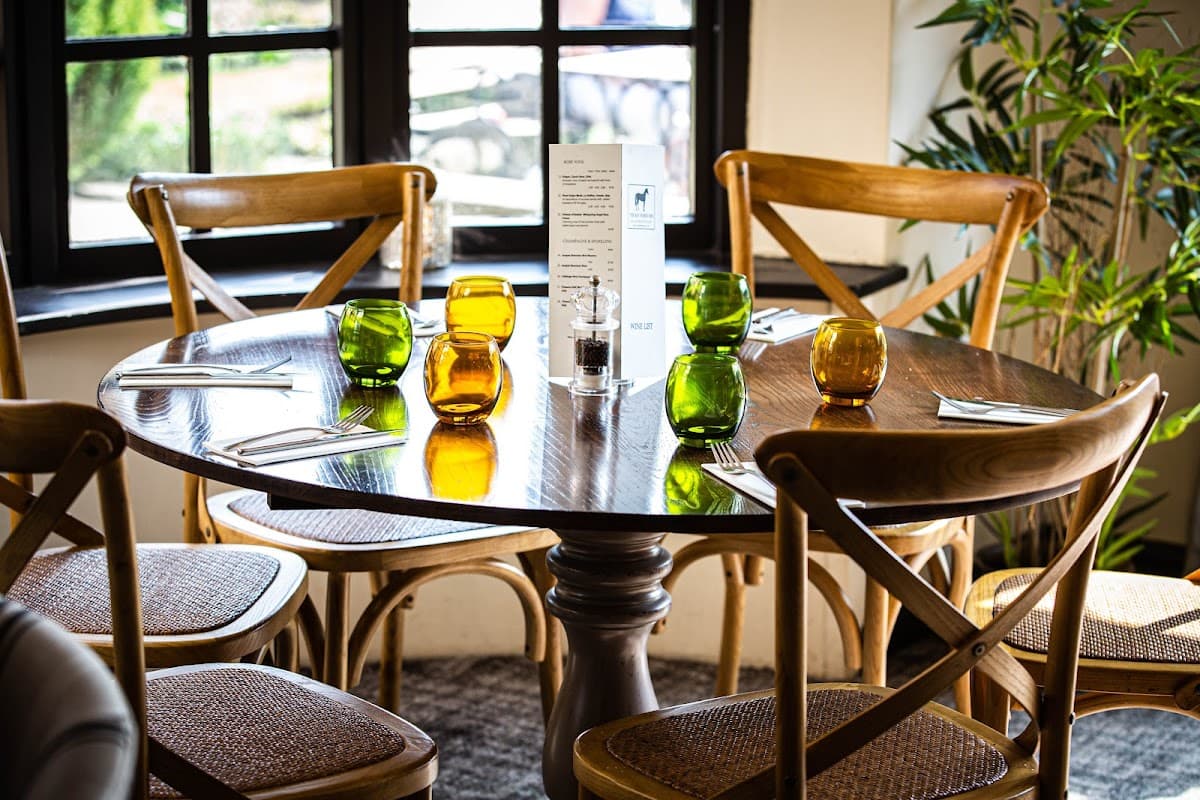 A wooden dining table set with colorful glassware and cutlery, surrounded by wooden chairs in a cozy restaurant setting.