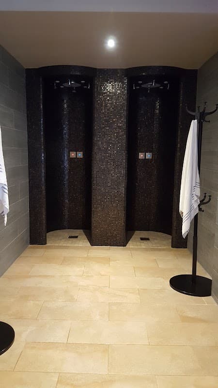 Luxurious shower area with dark tiled walls, two shower stalls, and hooks for towels on a stone floor.