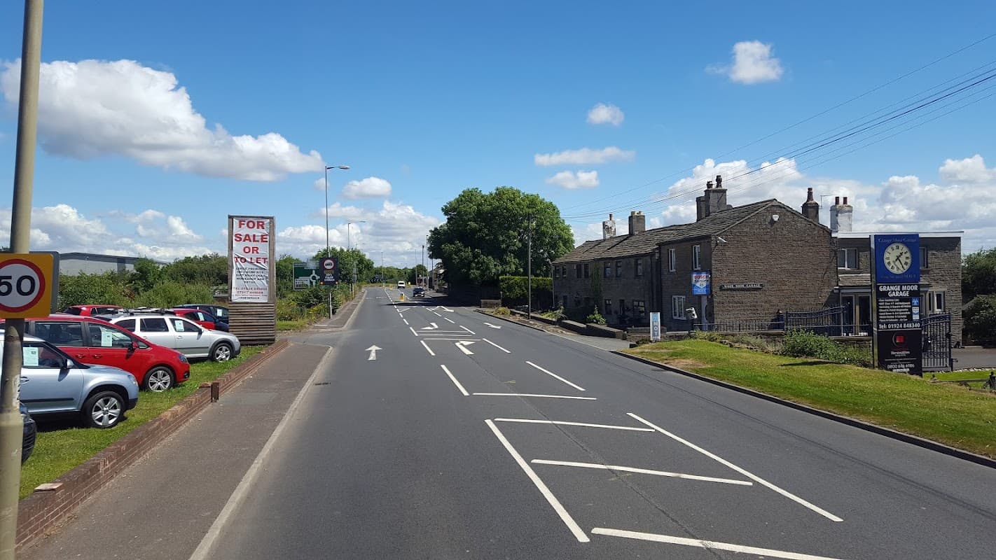 Grange Moor Garage Ltd on a sunny day, with cars parked and a "For Sale or Rent" sign visible.