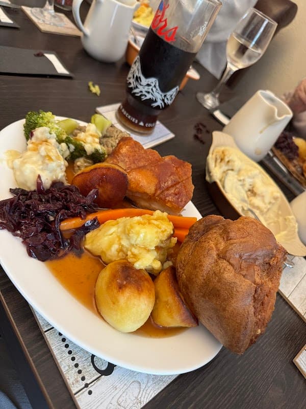 A plate of roast dinner featuring Yorkshire pudding, vegetables, and gravy, alongside drinks on a table.