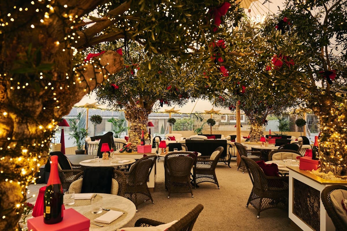 Cozy bar with olive trees adorned in lights, festive decor, and elegant seating in a warm, inviting atmosphere.