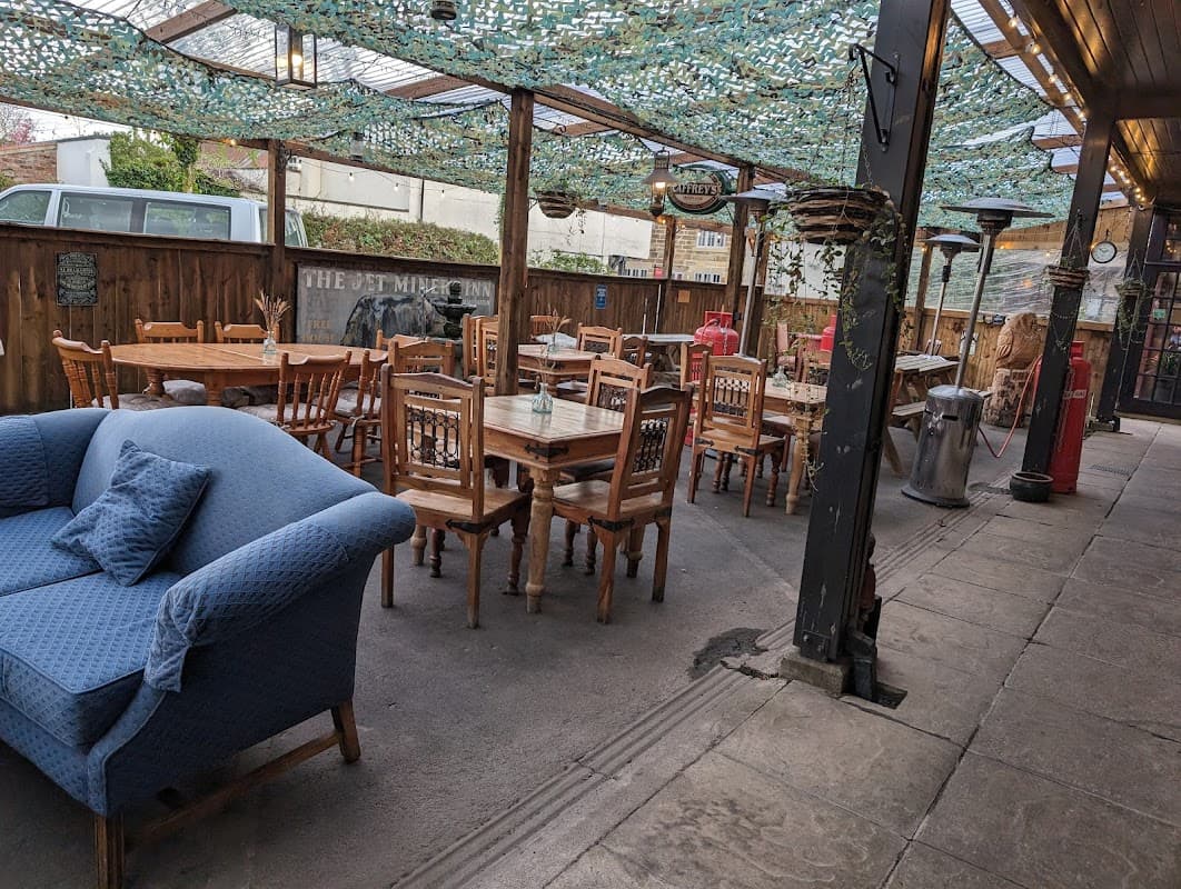 Outdoor seating area with wooden tables and chairs, a blue sofa, and a canopy overhead, in a rustic bar setting.