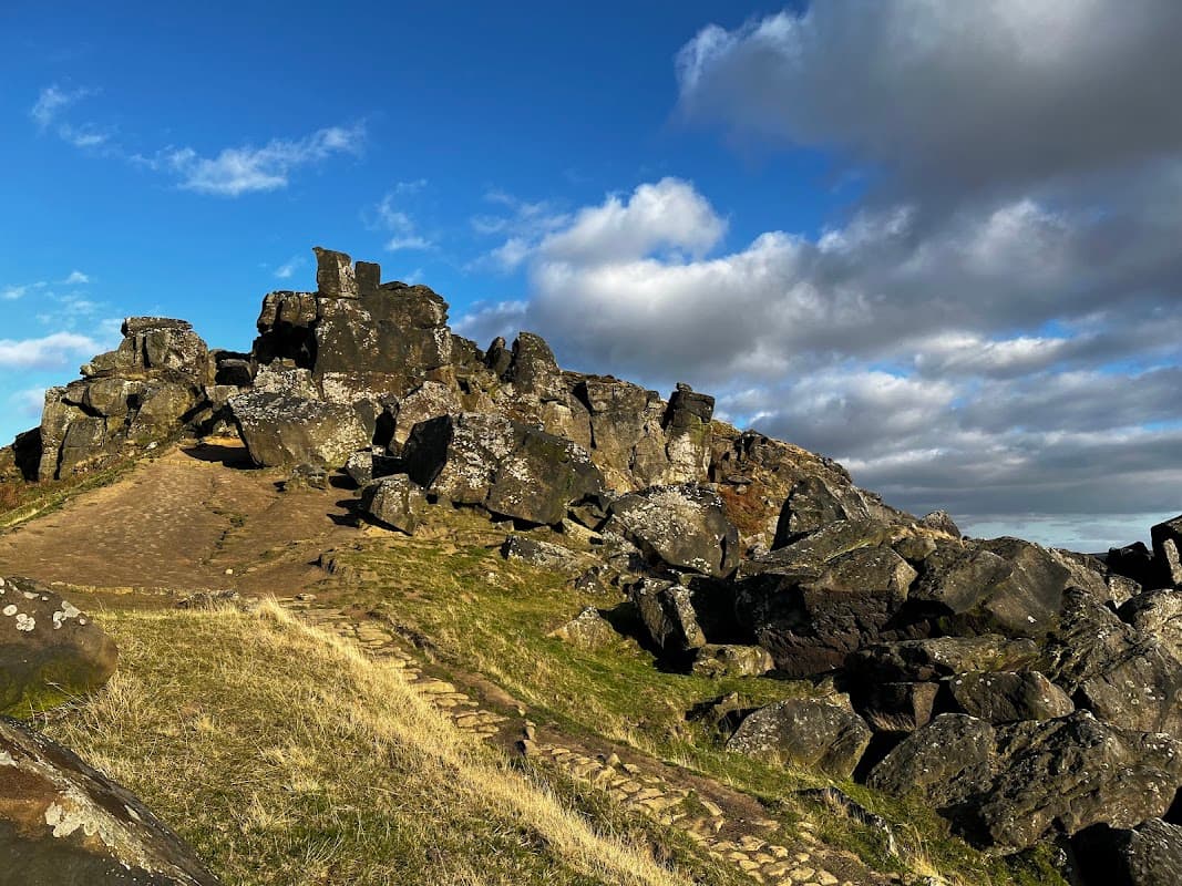 Rocky outcrop at The Wainstones, with a grassy path under a blue sky dotted with clouds in North Yorkshire.