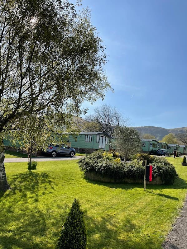 Lush green lawn with holiday caravans, trees, and a clear blue sky at Toft Hill Country Holiday Park in North Yorkshire.