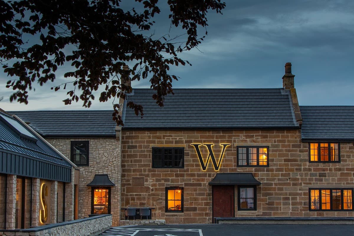 Wainstones Hotel features a stone facade with illuminated letters, warm windows, and a cloudy evening sky.