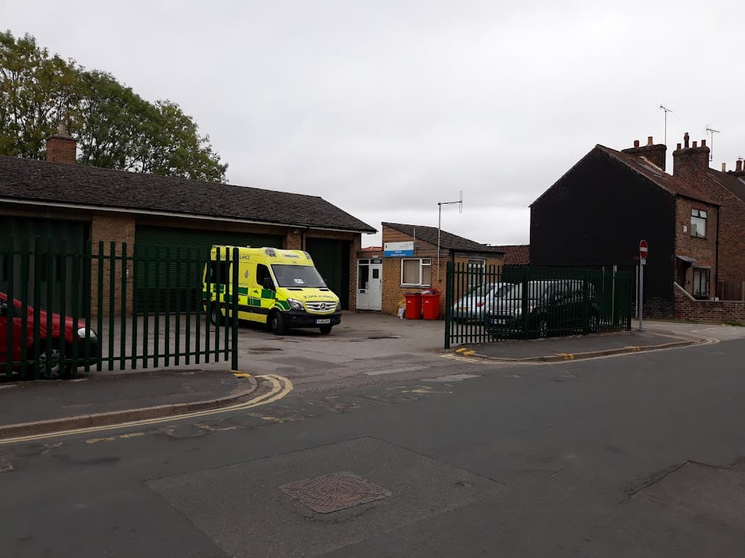 Ambulance station with a parked ambulance, nearby cars, and a gated entrance in a residential area.
