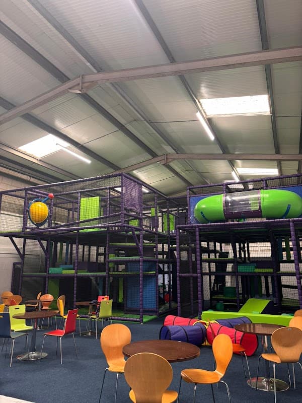 Colorful indoor soft play area with climbing frames, slides, and seating for kids and parents in a spacious setting.