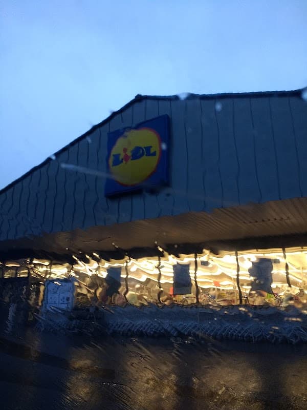 Lidl storefront with illuminated interior, seen through rain-streaked glass in a twilight setting.