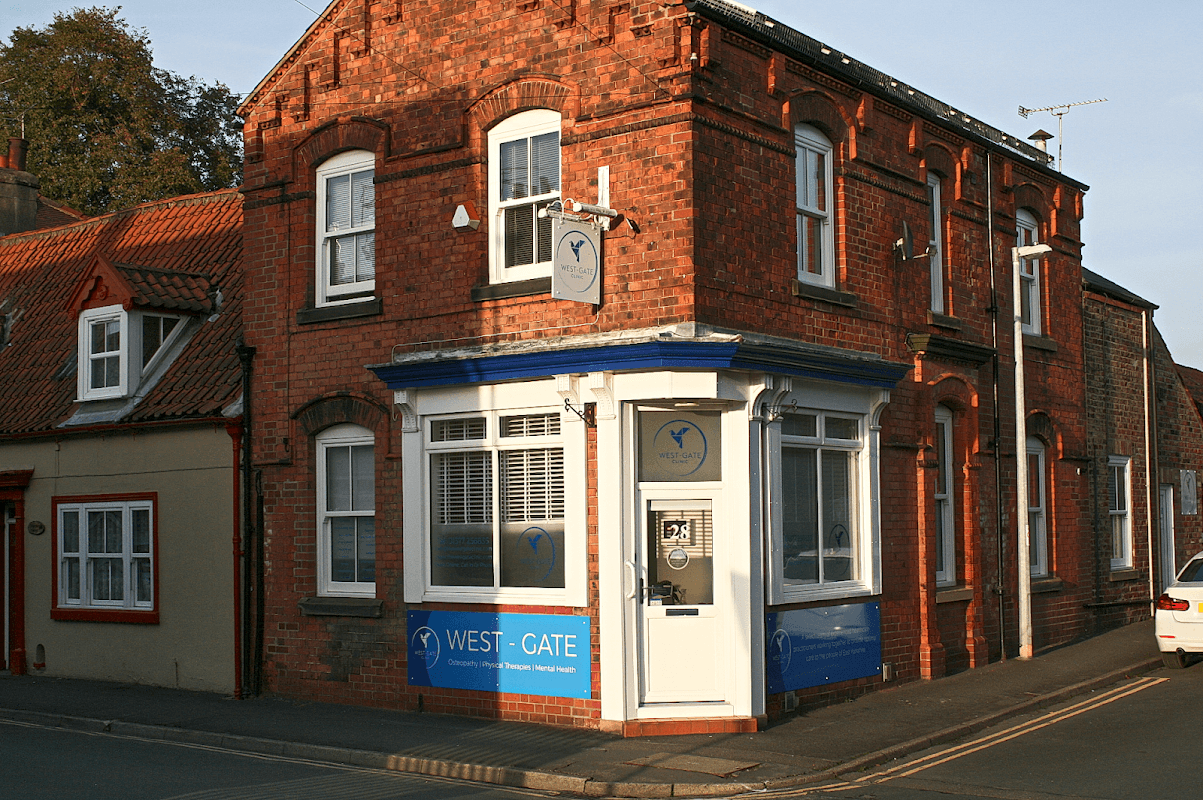 Brick building with a blue and white sign reading "WEST-GATE" and large windows, located on a street corner in Great Driffield.