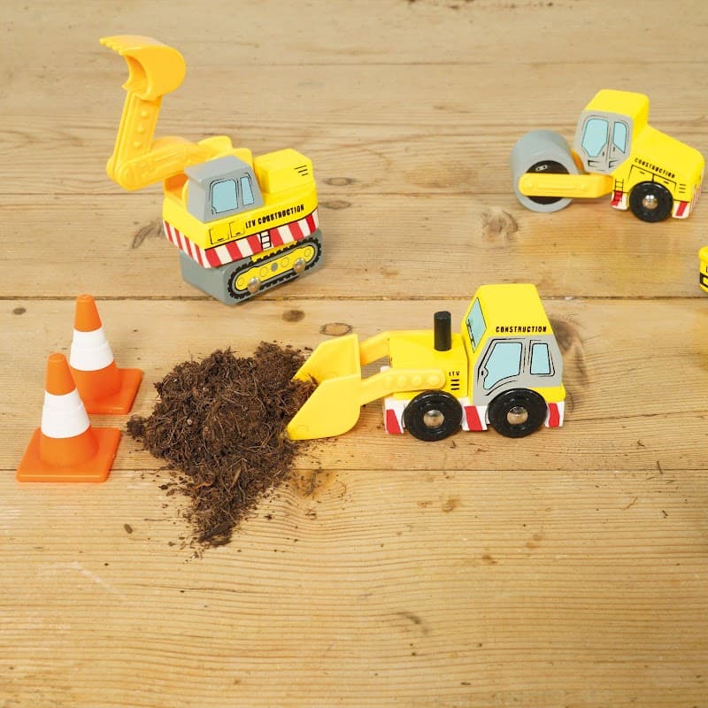 Toy construction vehicles, traffic cones, and a pile of dirt on a wooden surface.