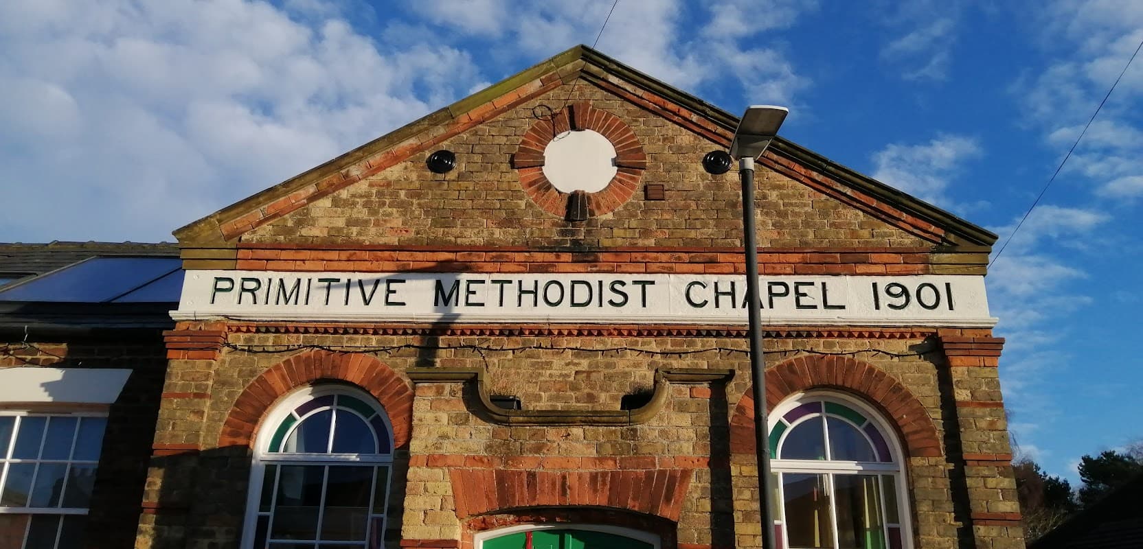 Historic brick building featuring "Primitive Methodist Chapel 1901" sign, with large windows and a clear blue sky.