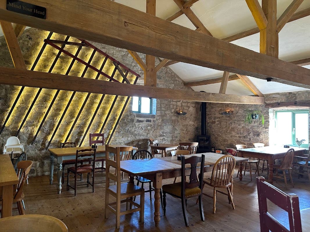 Rustic restaurant interior with wooden beams, stone walls, and empty tables surrounded by chairs in a cozy atmosphere.