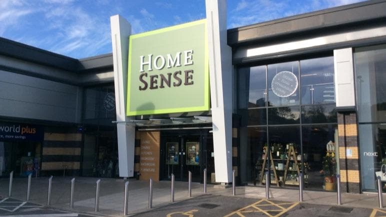 Entrance of Homesense store with a large green sign, modern architecture, and clear blue sky above.