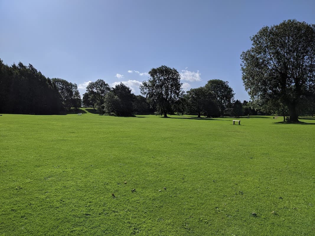 Lush green grass stretches across Nunroyd Park, dotted with trees under a bright blue sky.
