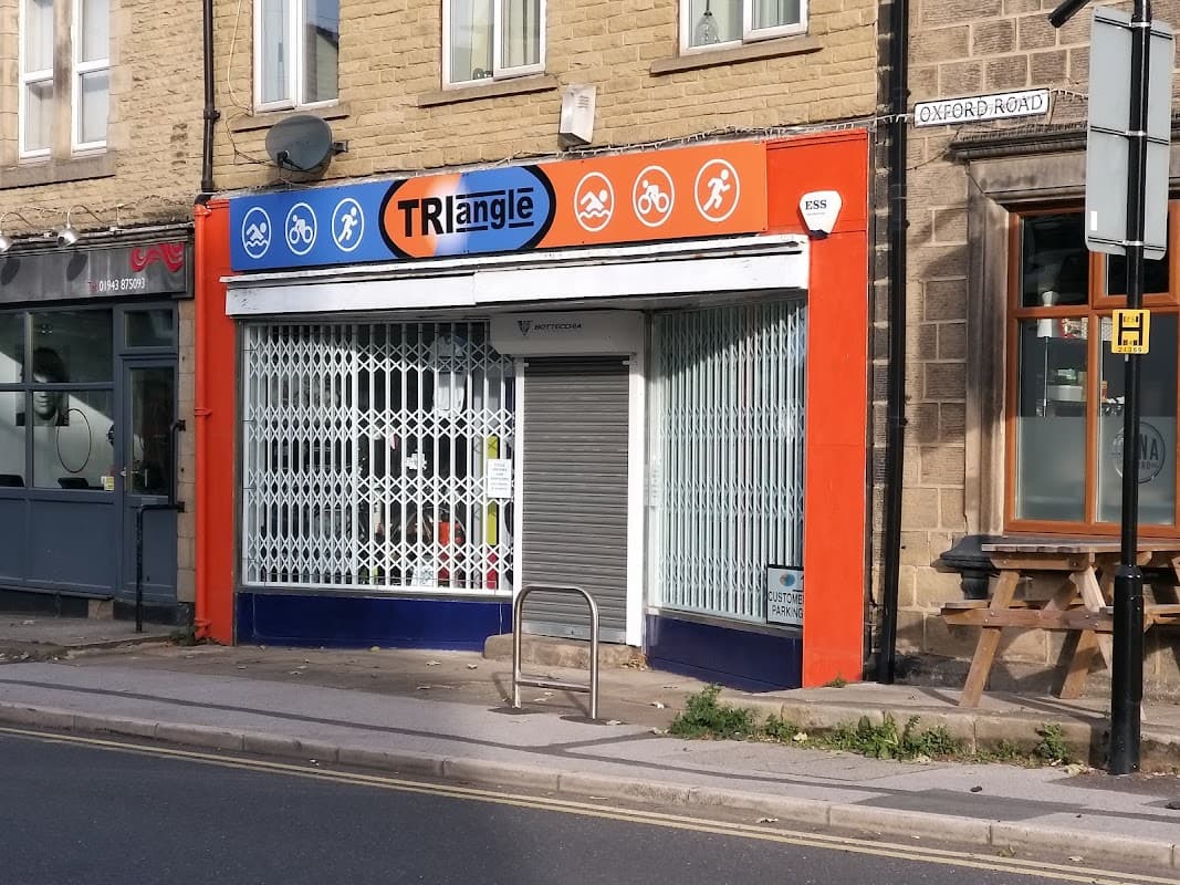 Bicycle shop with a colorful sign featuring bike icons, a closed shutter, and a bike rack outside on a street.